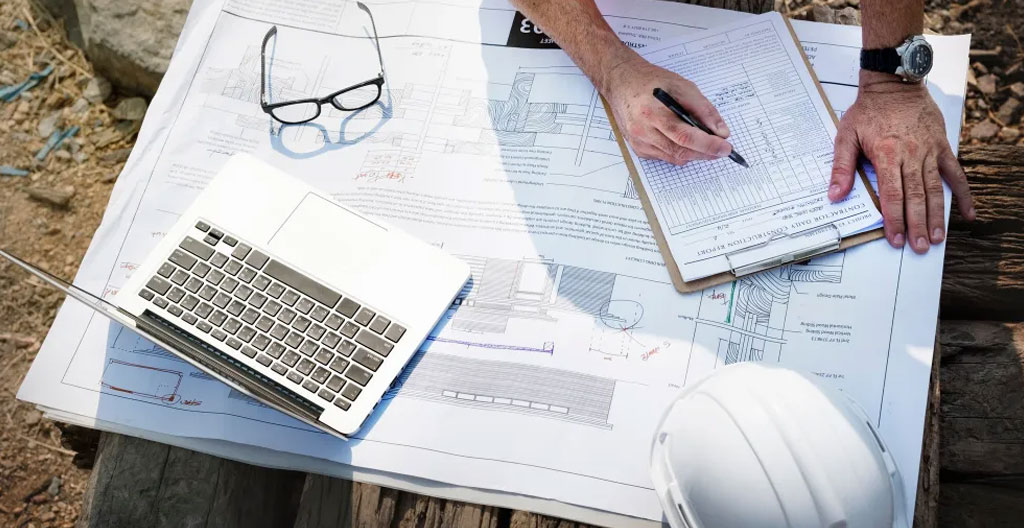 Entrepreneur et propriétaire debout sur un chantier résidentiel, consultant un calendrier de travaux sur tablette