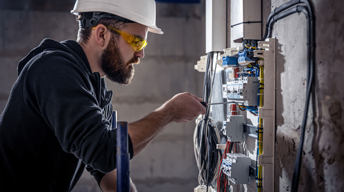 Panneau électrique résidentiel obsolète de 100 ampères ouvert montrant disjoncteurs vieillissants, avec main gantée d'inspecteur examinant l'installation